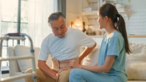 man recovering from back surgery at home with help of an assistant