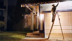 woman on a ladder hanging Christmas lights on the roof